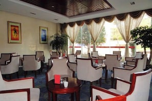 A hotel lobby with multiple seating areas, including round tables and chairs, and a large window with curtains. - Shuang Bai Hotel (Shuangbai)