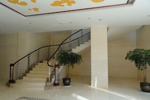 A hotel lobby with a marble staircase, potted plants, and a geometric ceiling design.