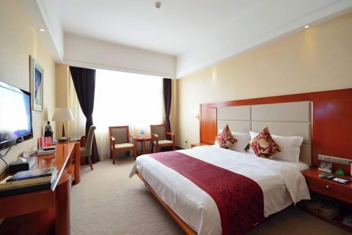 Una habitación de hotel con cama, escritorio, silla, televisor y ventana.