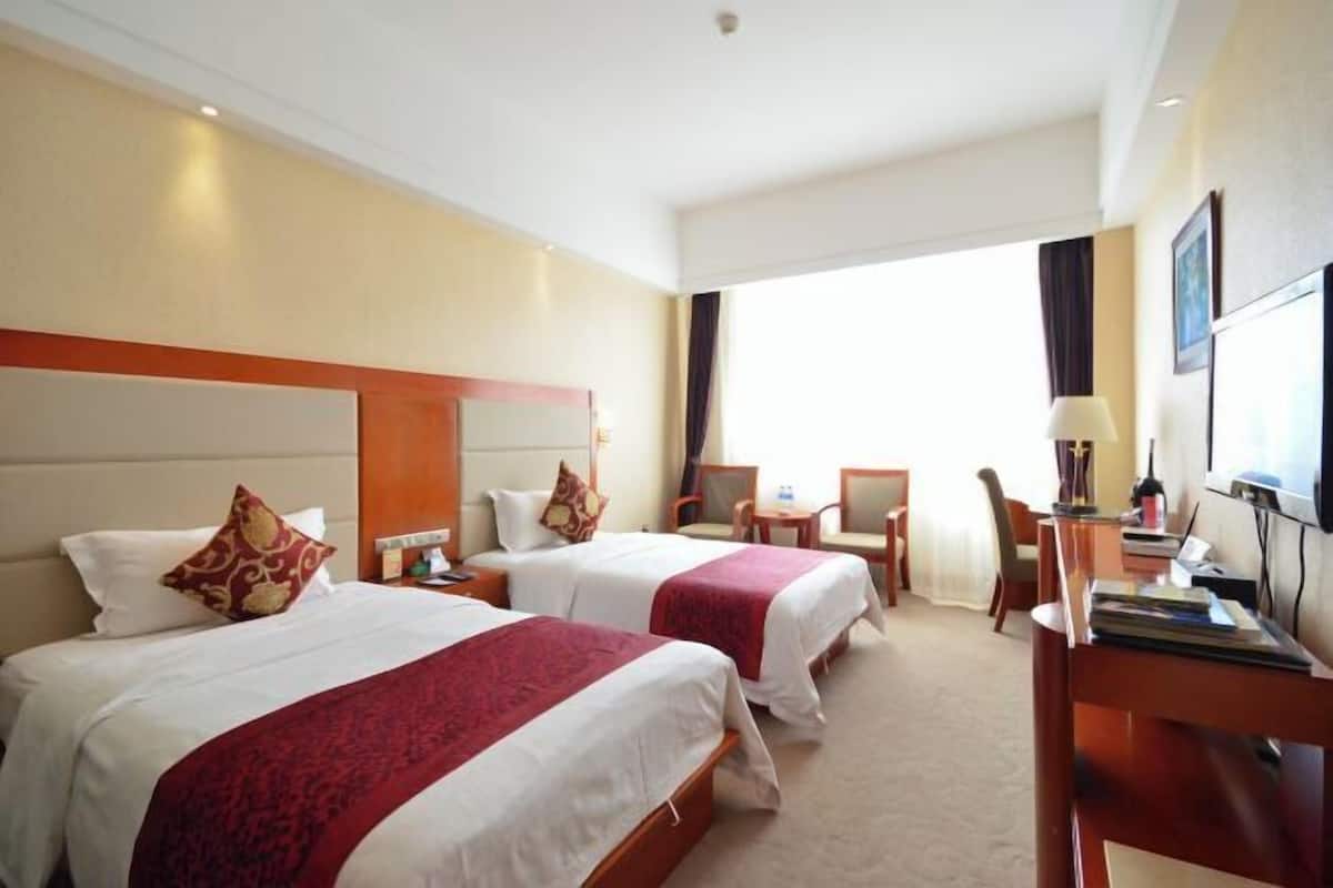 Habitación de hotel con dos camas, un escritorio, una silla y un ventanal grande.