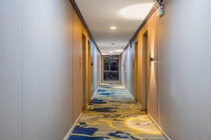 A hotel hallway with carpeted flooring, doors on both sides, and a light fixture on the ceiling.