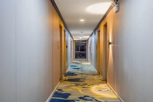 Un pasillo de hotel con suelo alfombrado, puertas a ambos lados y una lámpara en el techo.