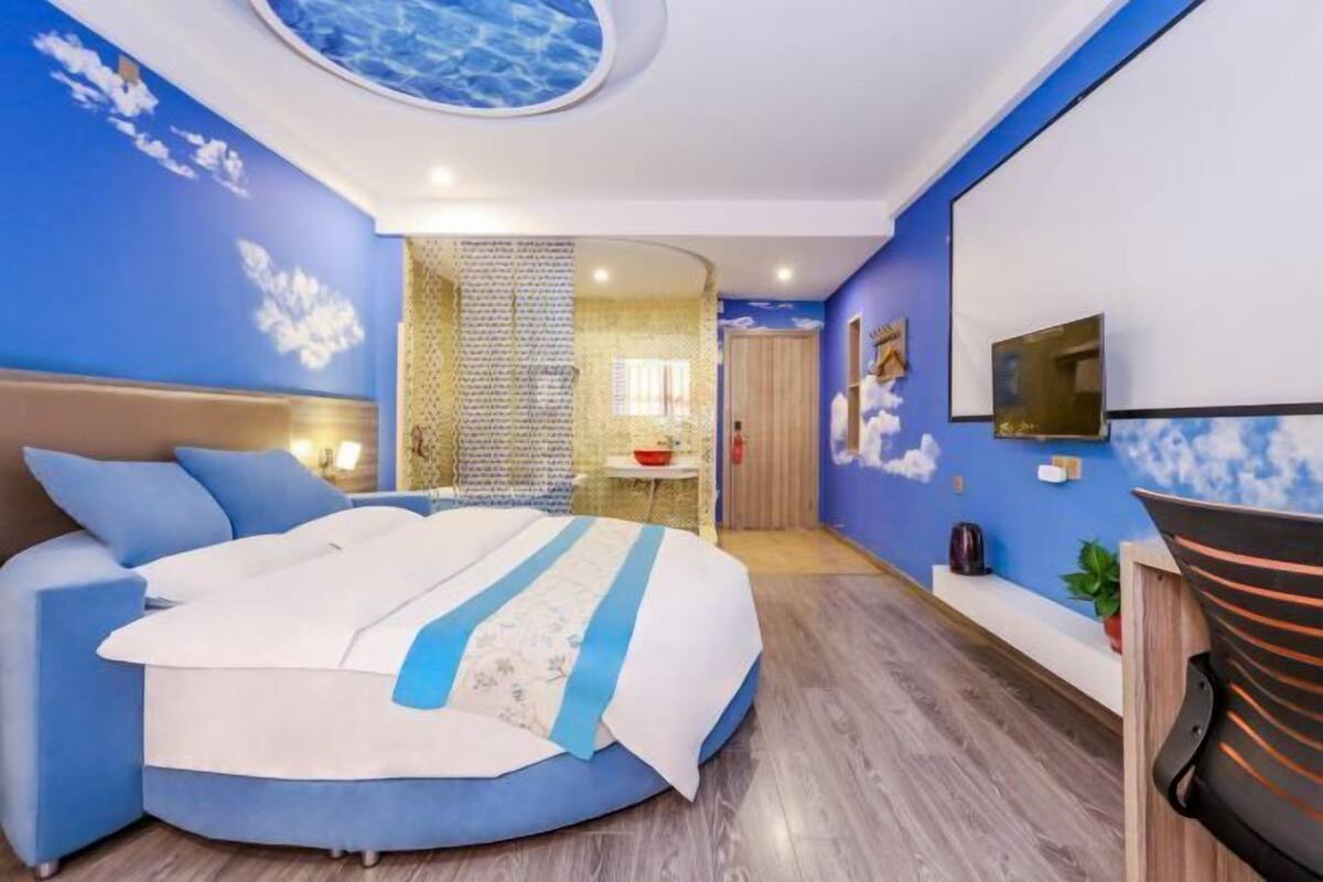 Ein modernes Schlafzimmer mit einem runden Bett, einem Fernseher und einem durch eine Glastür einsehbaren Badezimmer.