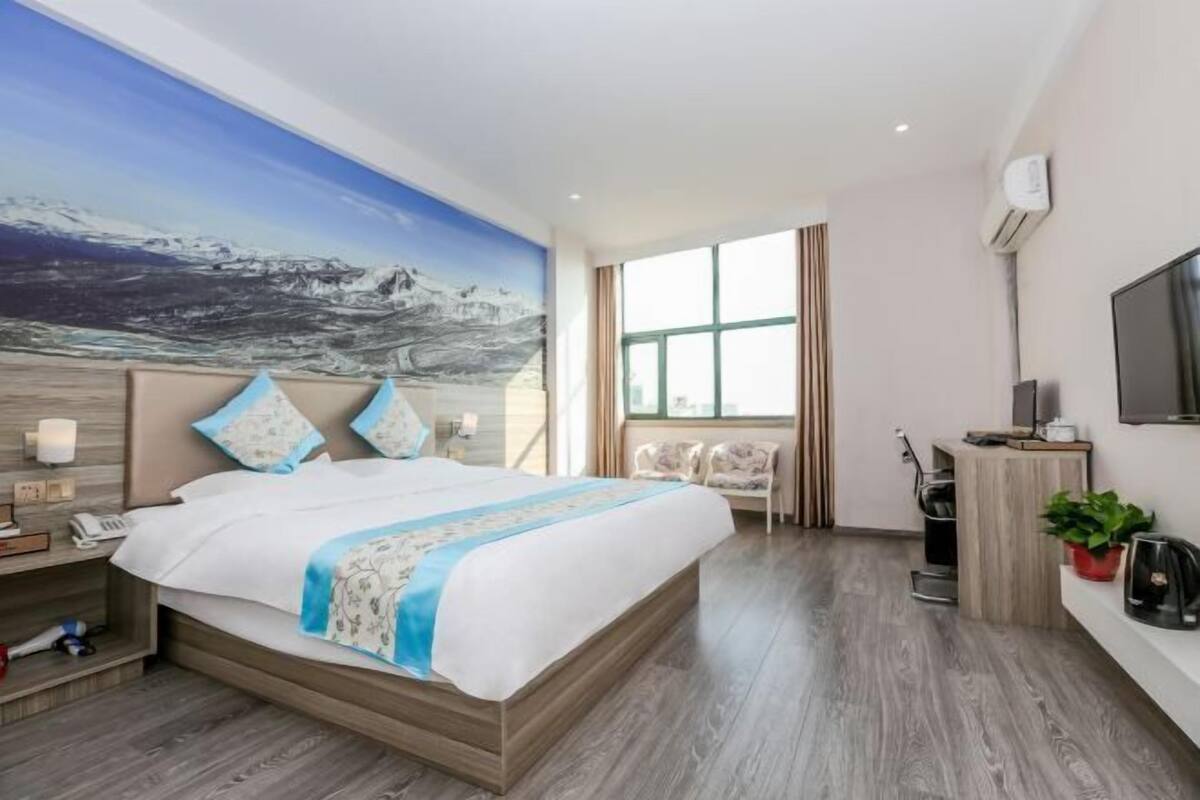 Ein modernes Hotelzimmer mit einem großen Bett, einem Bild an der Wand, einem Fernseher und einem Schreibtisch mit einer Pflanze.