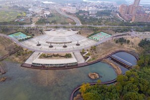 Vista aérea de un gran complejo de edificios circulares con un espacio abierto central, rodeado de cuerpos de agua y vegetación.