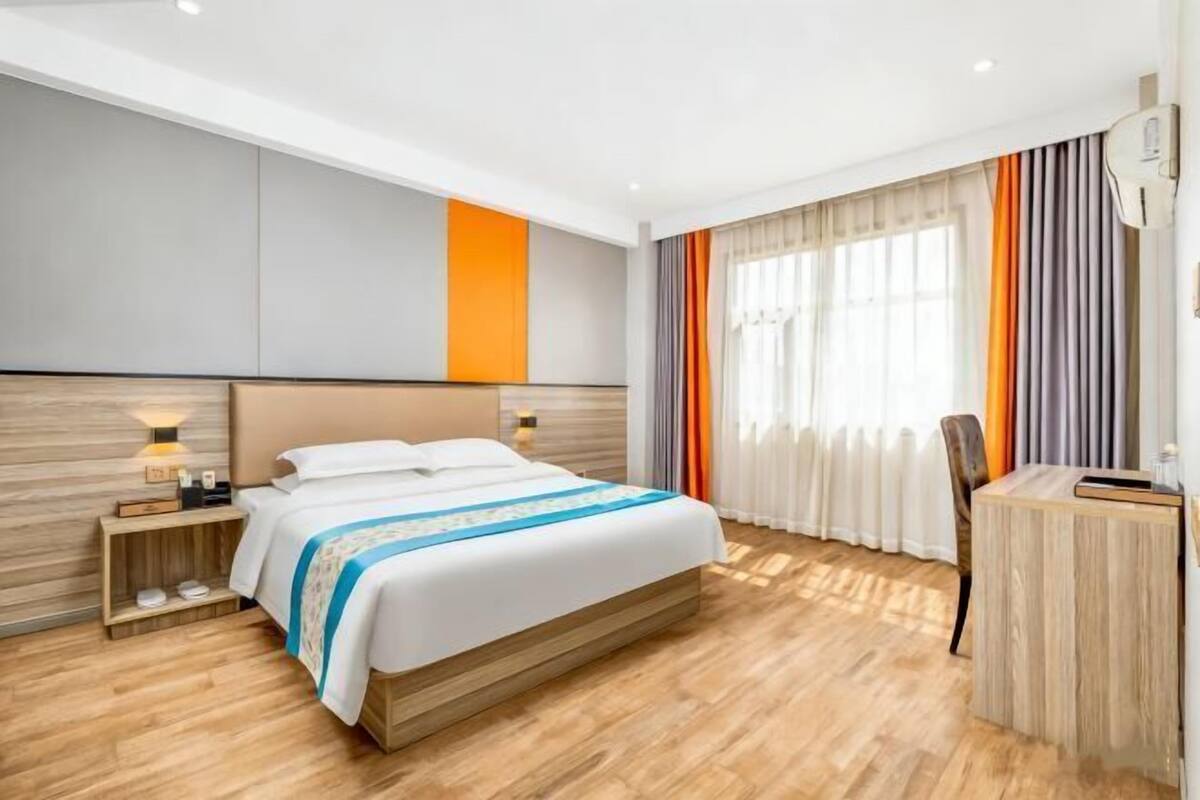 Ein modernes Hotelzimmer mit einem großen Bett, einem Holzkopfstück, einem Schreibtisch und einem Fenster mit Vorhängen.