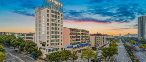 A multi-story hotel with a modern design, located at a city intersection with wide roads and greenery.