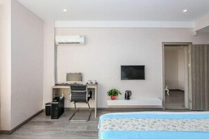 Una habitación de hotel moderna con una cama, un escritorio con una silla, un televisor, una pequeña planta y un equipo de aire acondicionado.