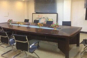 Un salón de conferencias con una larga mesa, sillas y un arreglo floral.