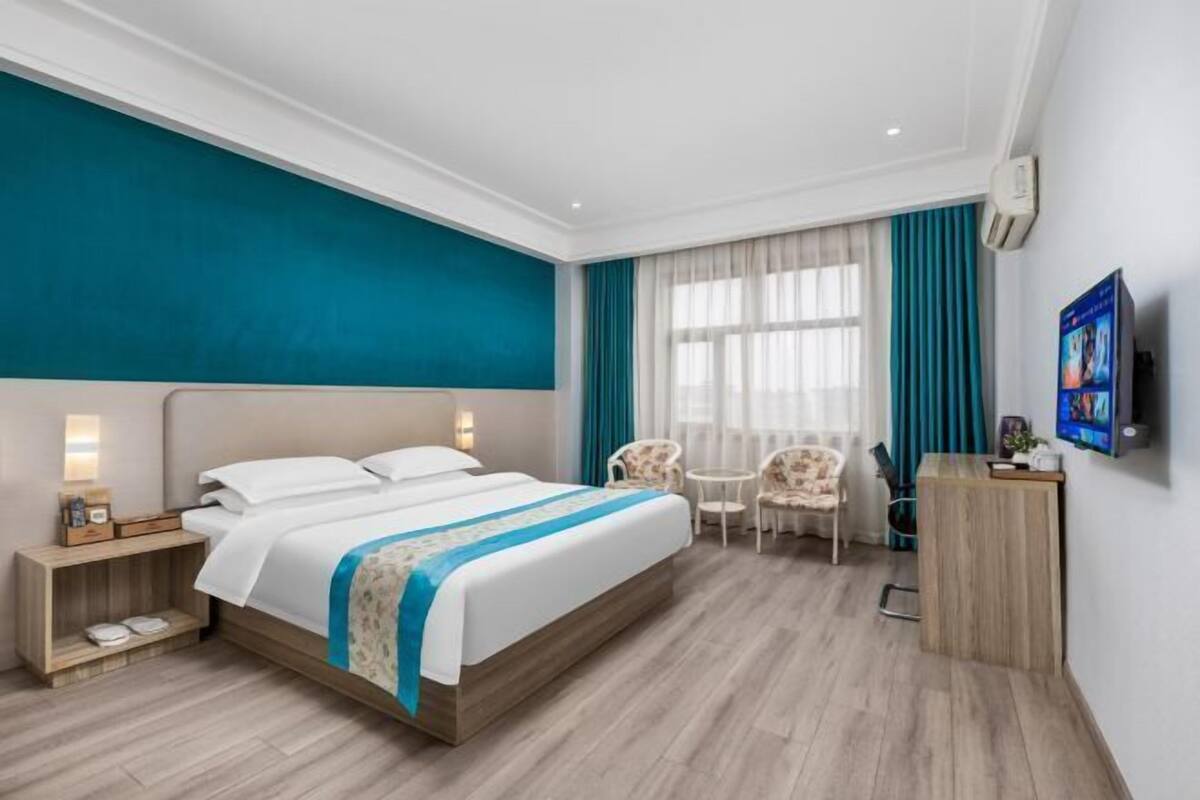 Ein Hotelzimmer mit einem großen Bett, einem Schreibtisch, einem Sessel, einem Fernseher und einem Fenster mit Vorhängen.