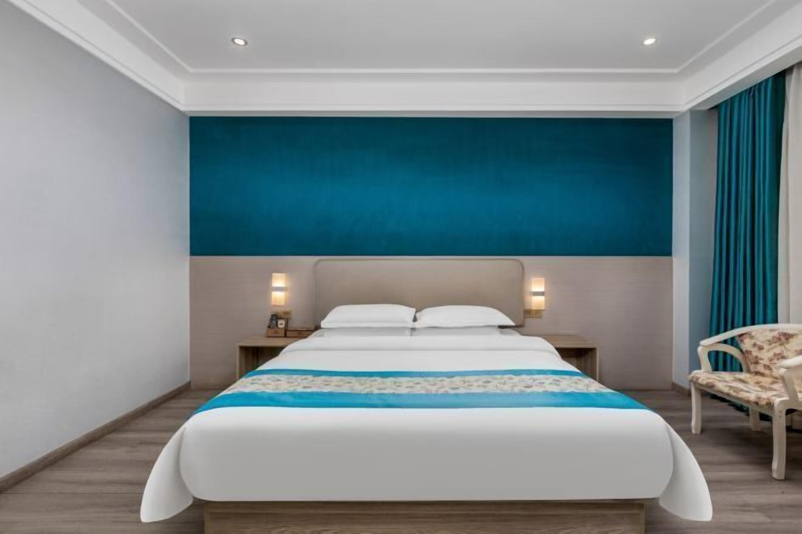 A modern hotel room with a large bed, two bedside tables, and a chair.