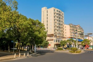 Un hotel de varios pisos con una entrada destacada, rodeado de árboles y un cielo despejado.