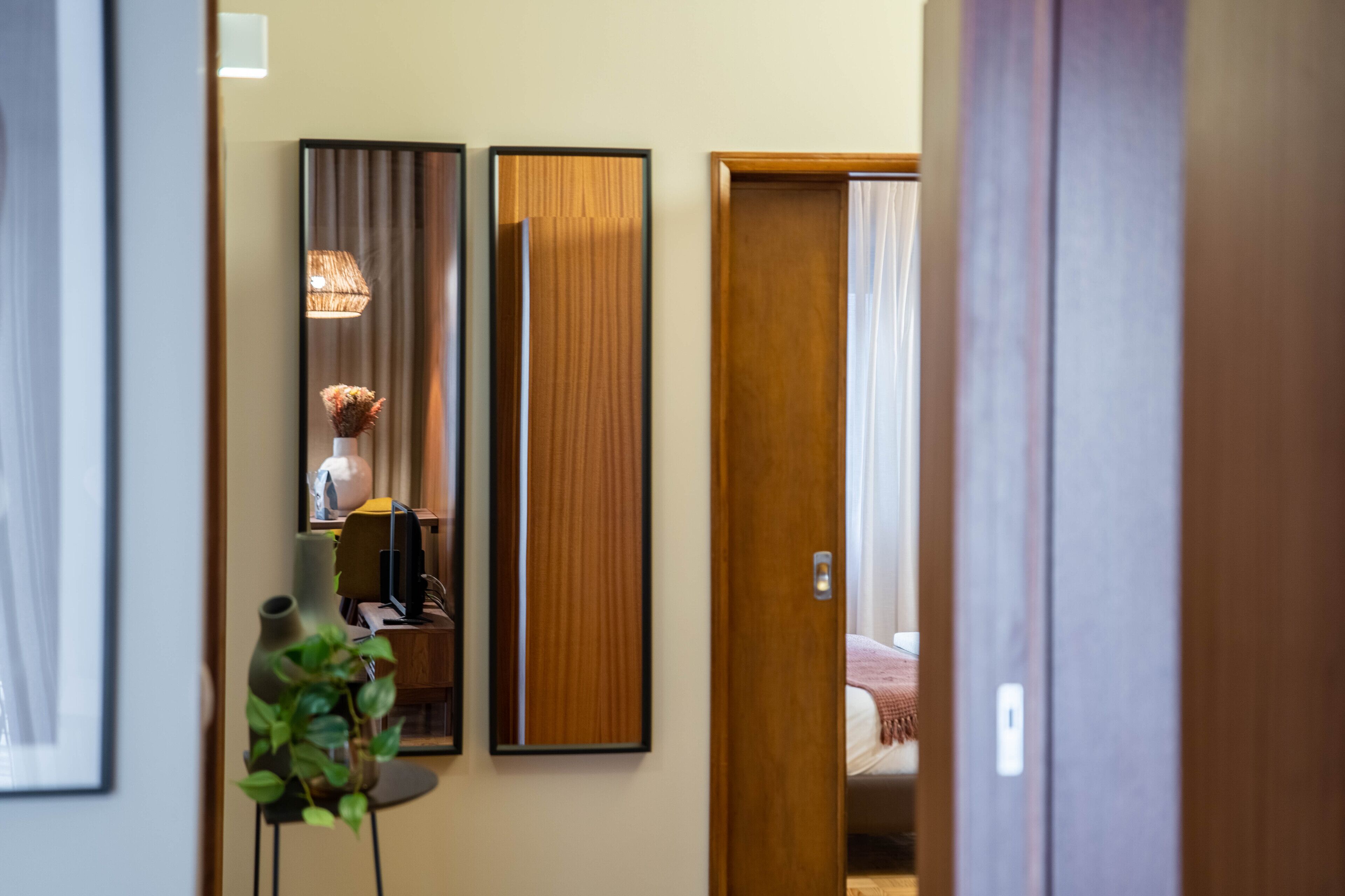 A hallway with a wooden door, a mirror, and a small table with a plant.