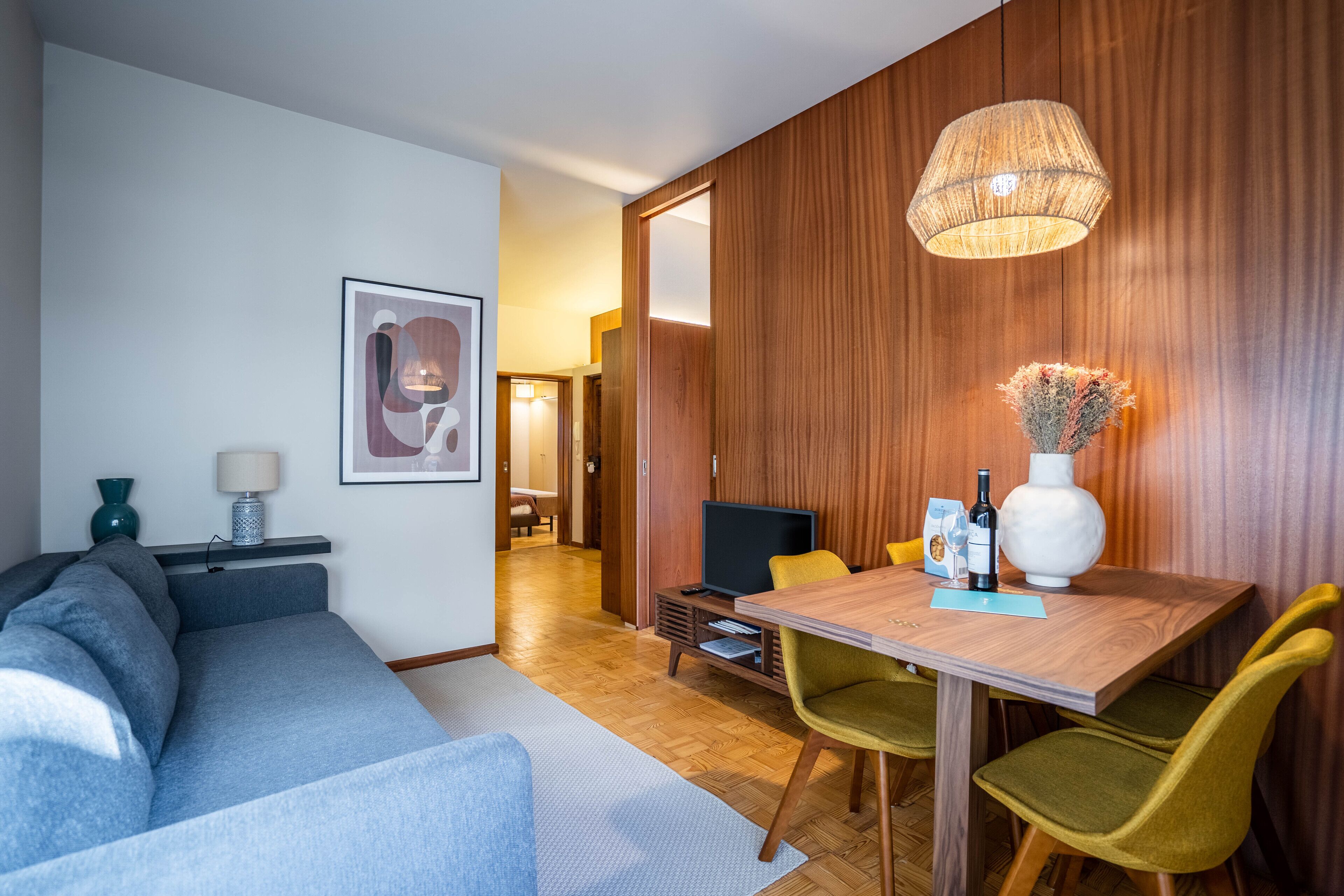 Een moderne woonkamer met een bank, een eettafel met stoelen, een televisie en een decoratieve vaas.