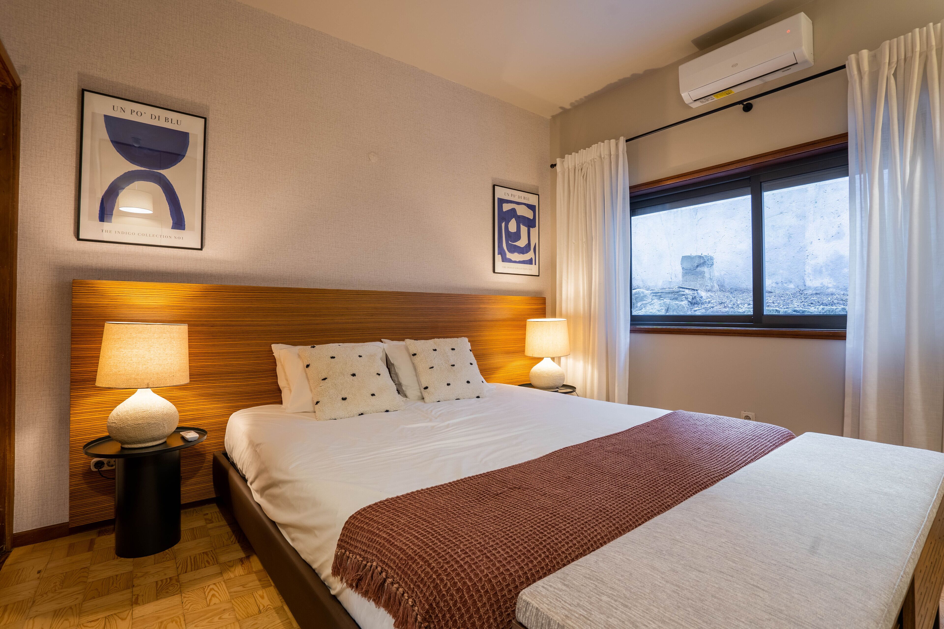 A neatly made bed with a wooden headboard, two bedside lamps, and a window with curtains.