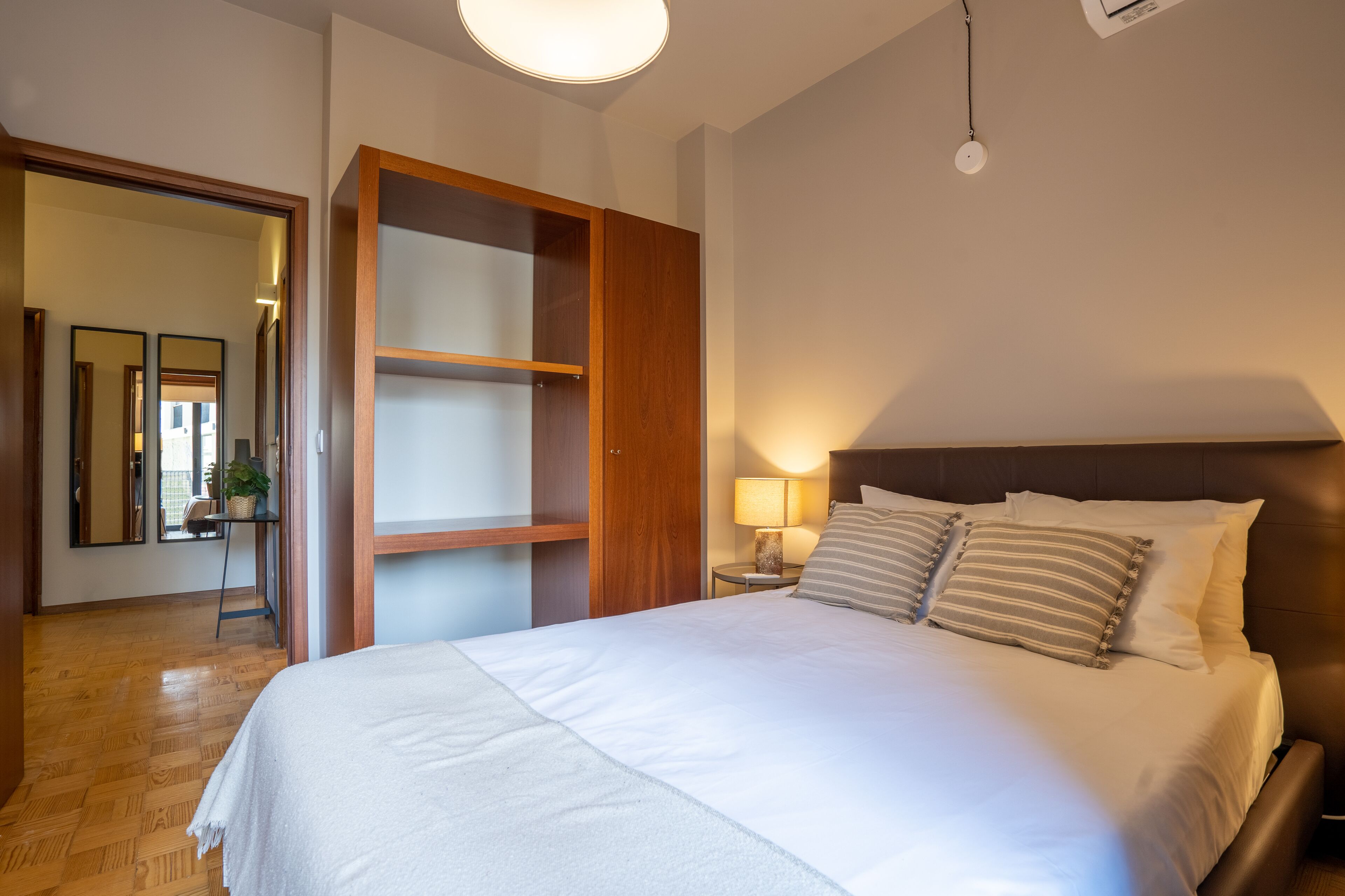 Ein Schlafzimmer mit einem großen Bett, einem Holzschrank, einem Nachttisch mit Lampe und einem Spiegel.