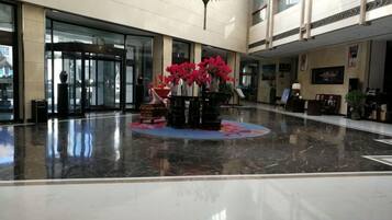 A spacious lobby with a marble floor, a reception desk, and a decorative centerpiece with flowers.
