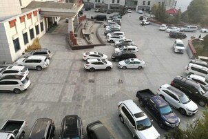 A parking lot with multiple cars parked in rows, a building with a flat roof and a few windows, and a clear sky.