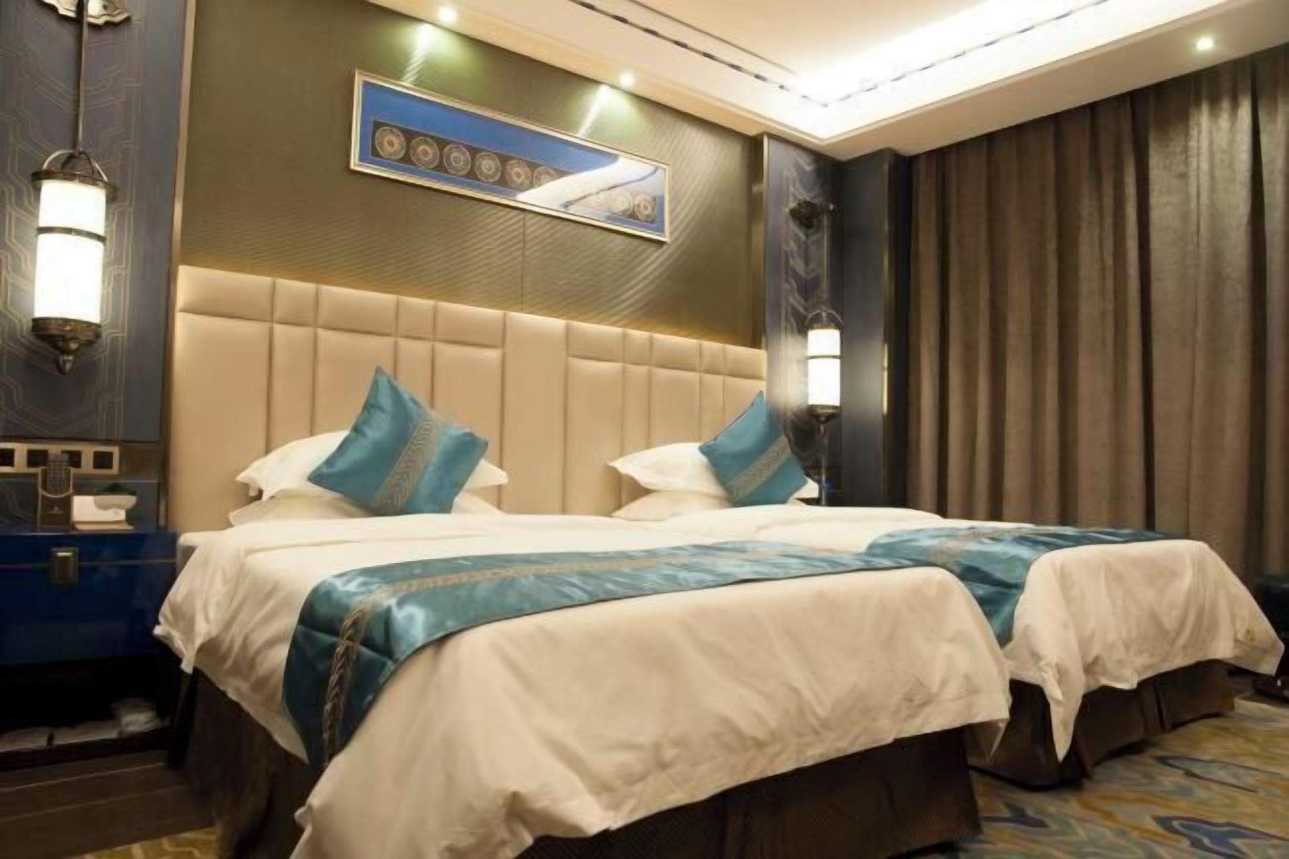 A hotel room with two beds, a headboard, wall-mounted lamps, a painting, and a curtain.