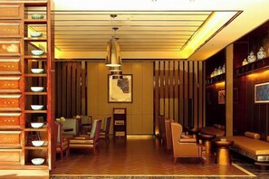 A hotel lobby with a wooden reception desk, seating area, and a large chandelier.