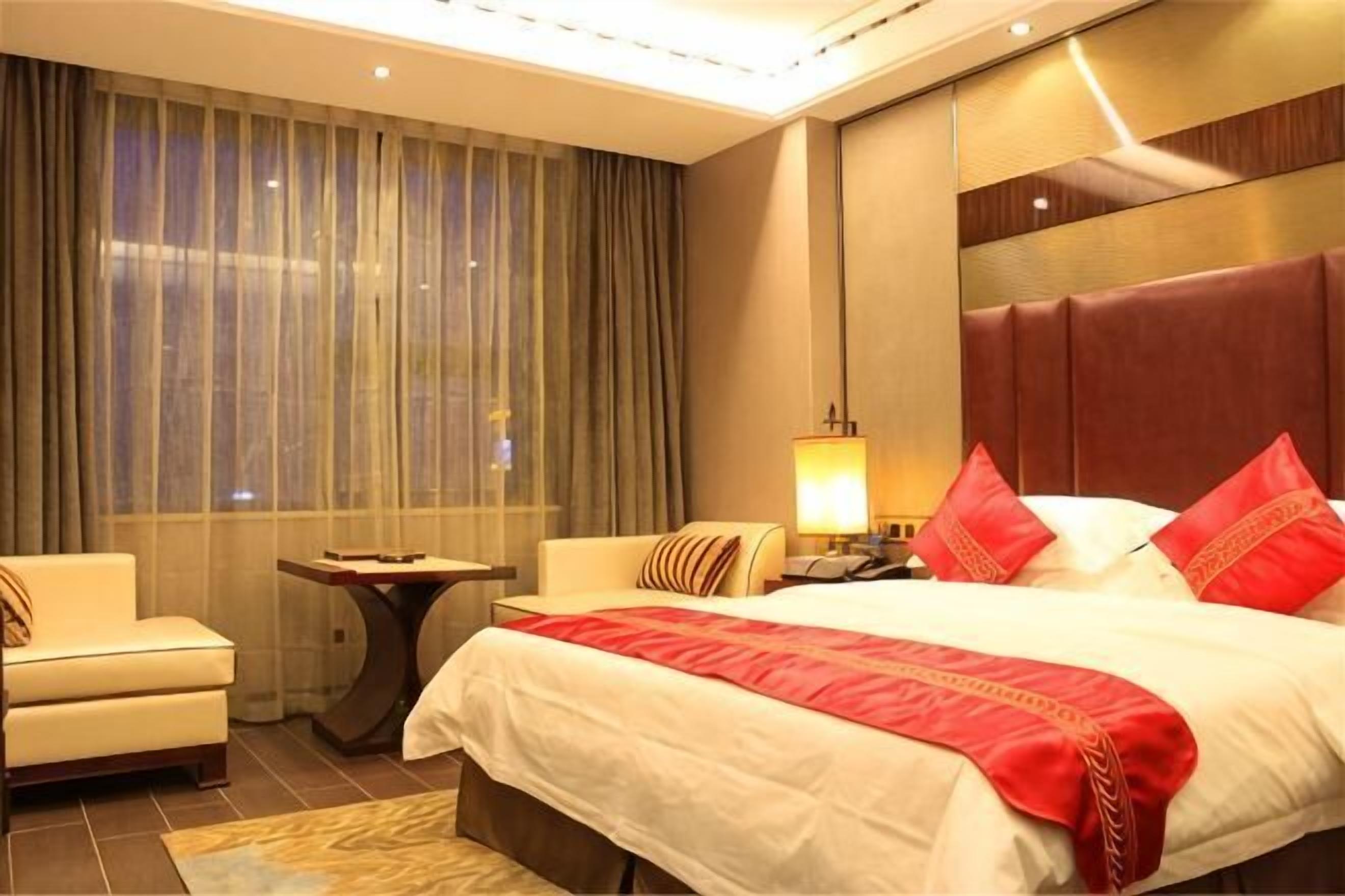 Habitación de hotel con una cama grande, una mesita de noche, una silla y una ventana con cortinas.