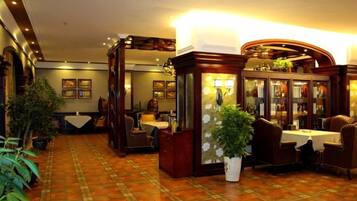 A hotel lobby with a checkered floor, a reception desk, and a seating area with tables and chairs.