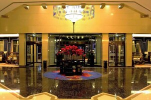 Un vestíbulo de hotel con piso de mármol pulido, un arreglo floral central y un candelabro.