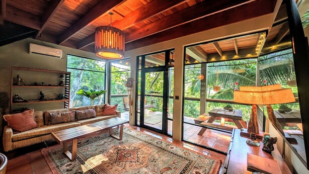 Uma sala de estar aconchegante com sofá, mesa de centro e uma grande janela com vista para o verde.