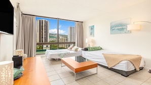 A hotel room with two beds, a wooden desk, a lamp, and a view of tall buildings.