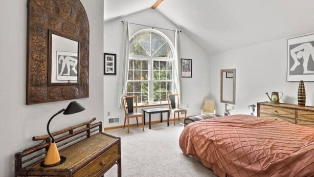 Ein Schlafzimmer mit einem großen Bett, einem Schreibtisch, einem Sessel, einem Fenster mit Aussicht und Bildern an den Wänden.