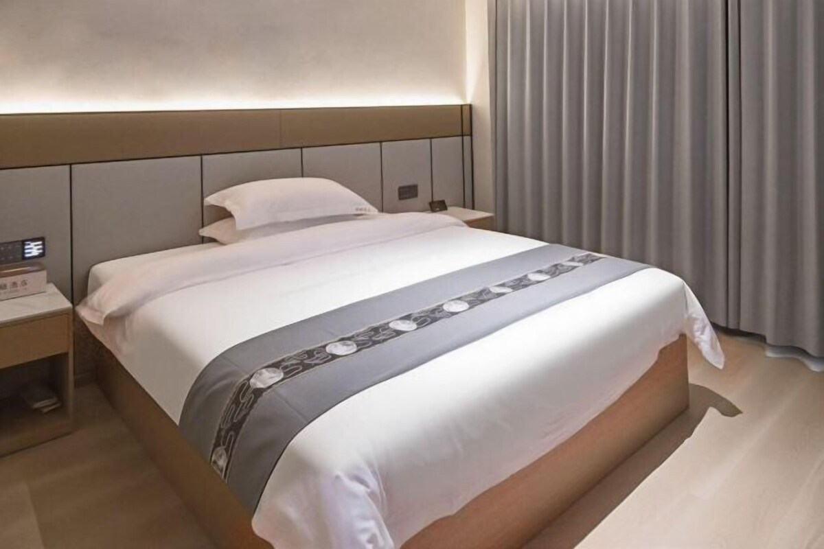 A hotel room with a bed, bedside tables, a nightstand, and a window with curtains.
