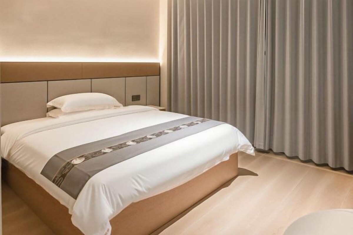 Quarto de hotel com cama, mesa de cabeceira e janela com cortinas.