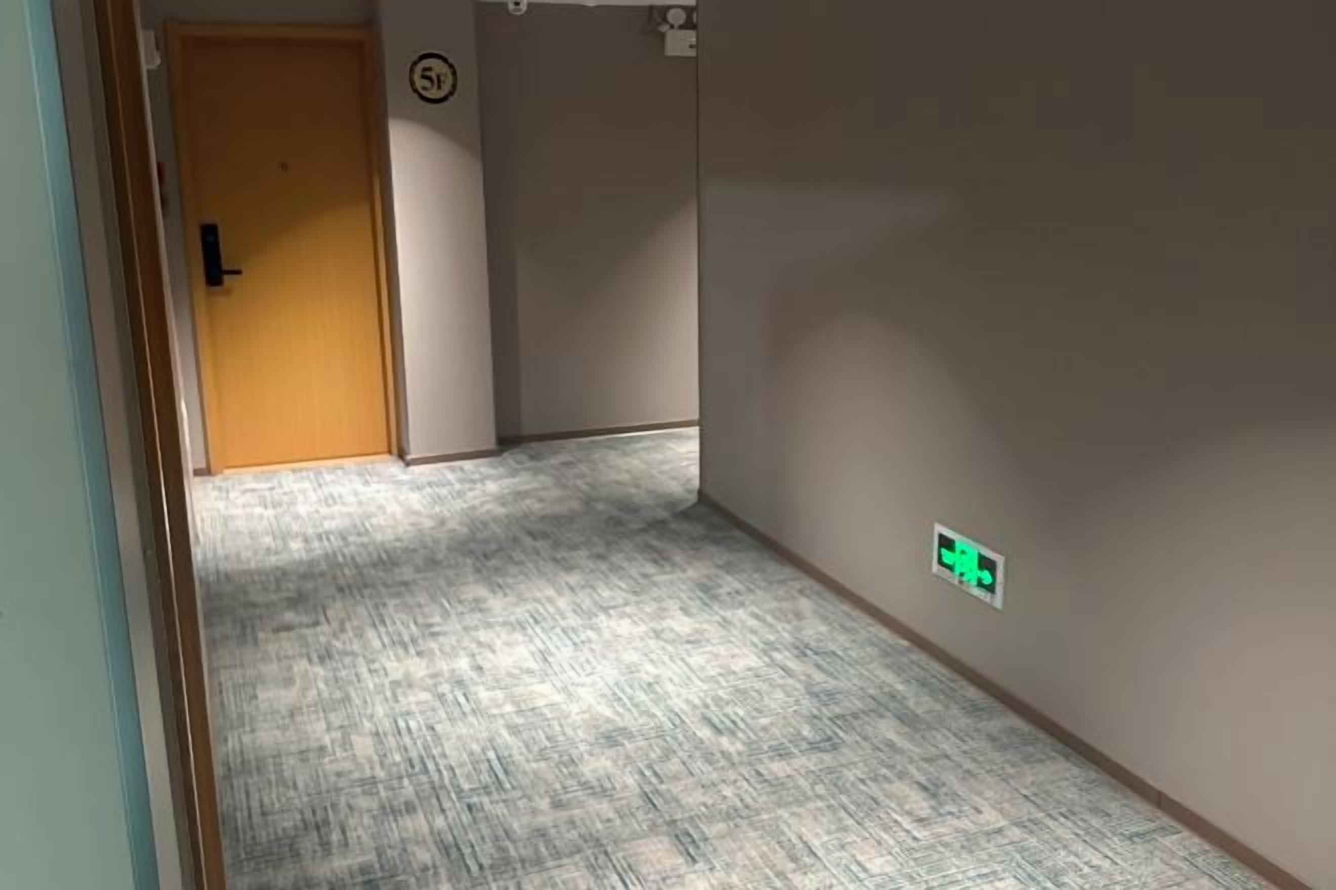 Un corridoio con pavimento rivestito di moquette, una porta e un cartello fissato al muro.
