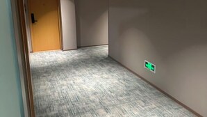 Um corredor com piso coberto de carpete, uma porta e uma placa fixada na parede.
