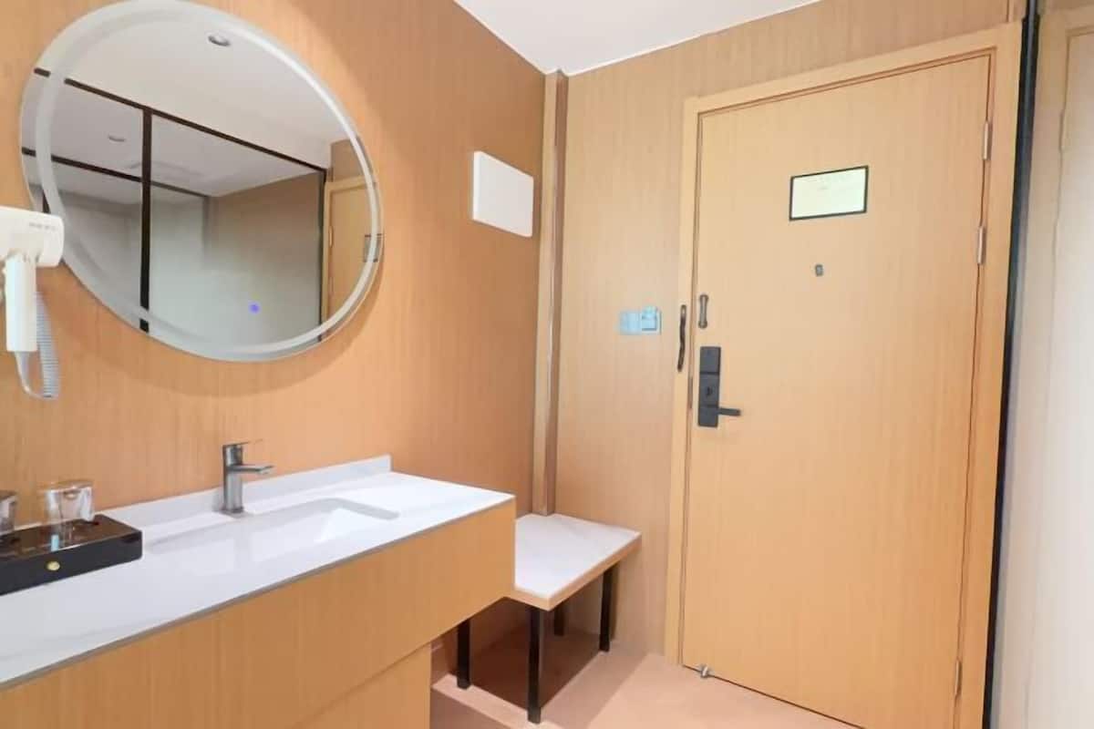 Ein Badezimmer mit rundem Spiegel, einem weißen Waschbecken, einer Holztür und einer kleinen Ablagefläche.