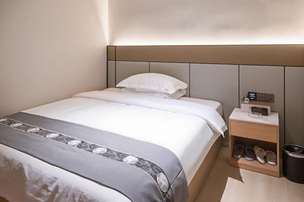 A hotel room with a bed, bedside table, and a shoe rack.