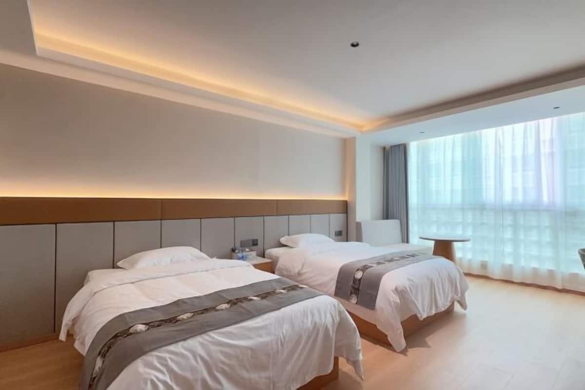 Ein Hotelzimmer mit zwei Betten, einem Nachttisch, einem Sessel und einem großen Fenster mit transparenten Vorhängen.