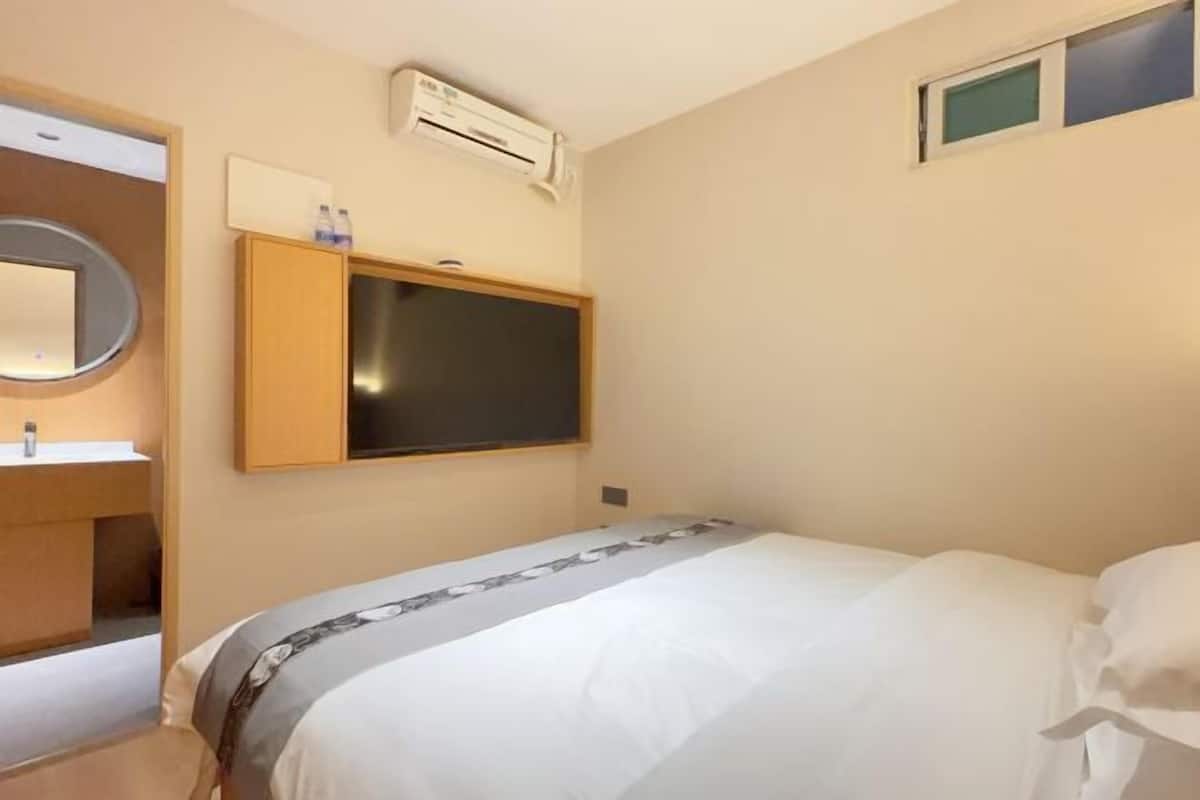 Ein Hotelzimmer mit Bett, integriertem Fernseher, kleinem Fenster und Klimaanlage.
