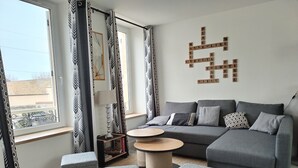 Ett modernt vardagsrum med en grå soffa, två gråa pallar, ett runt soffbord och en bokhylla.