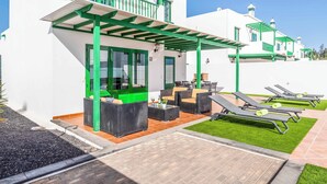 Un bâtiment blanc agrémenté de touches de vert, avec des places assises à l’extérieur et un espace patio.