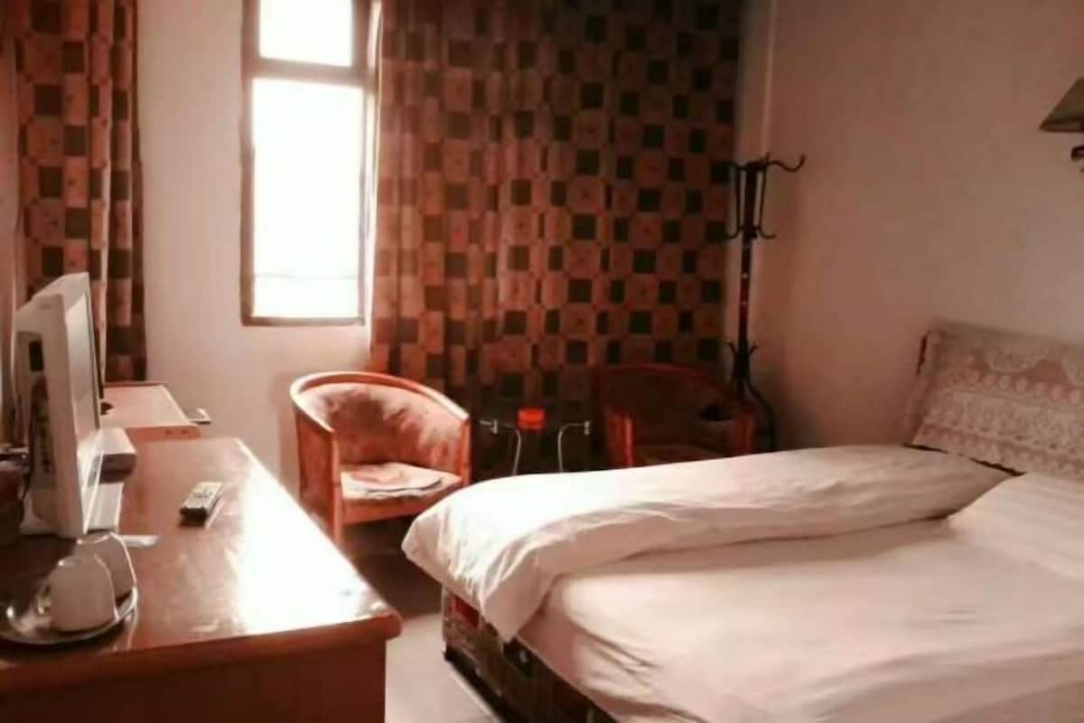 A hotel room with a bed, a desk with a computer, a chair, and a window with curtains.
