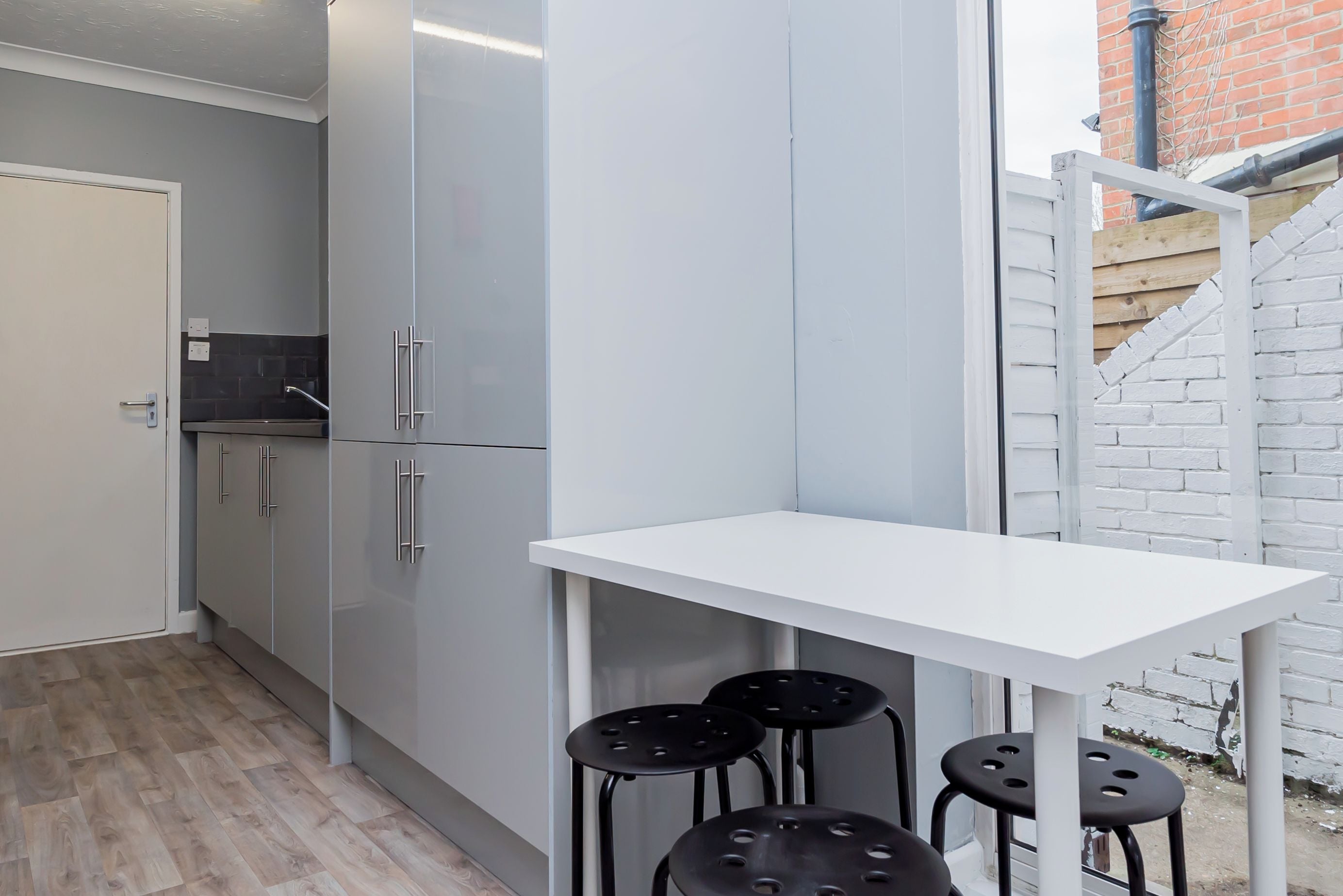 A compact kitchen with grey cabinets, a white countertop, and a small table with four black stools.