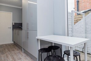 A compact kitchen with grey cabinets, a white countertop, and a small table with four black stools. - Shirley House 2 Guest House Self Catering by Southampton General Hospital  (Southampton)
