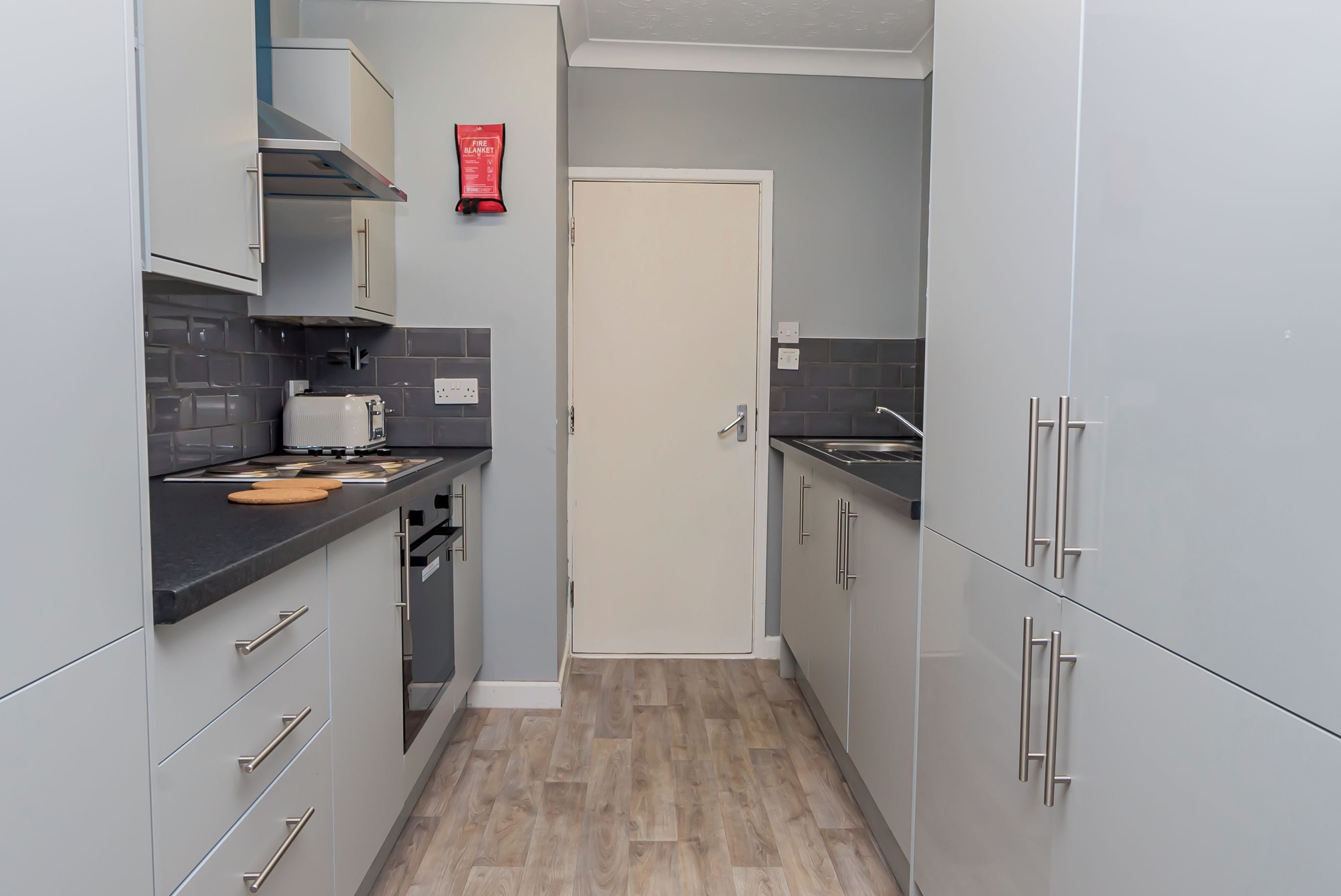 Una cucina compatta con mobili grigi, un tostapane e una coperta antincendio appesa al muro.