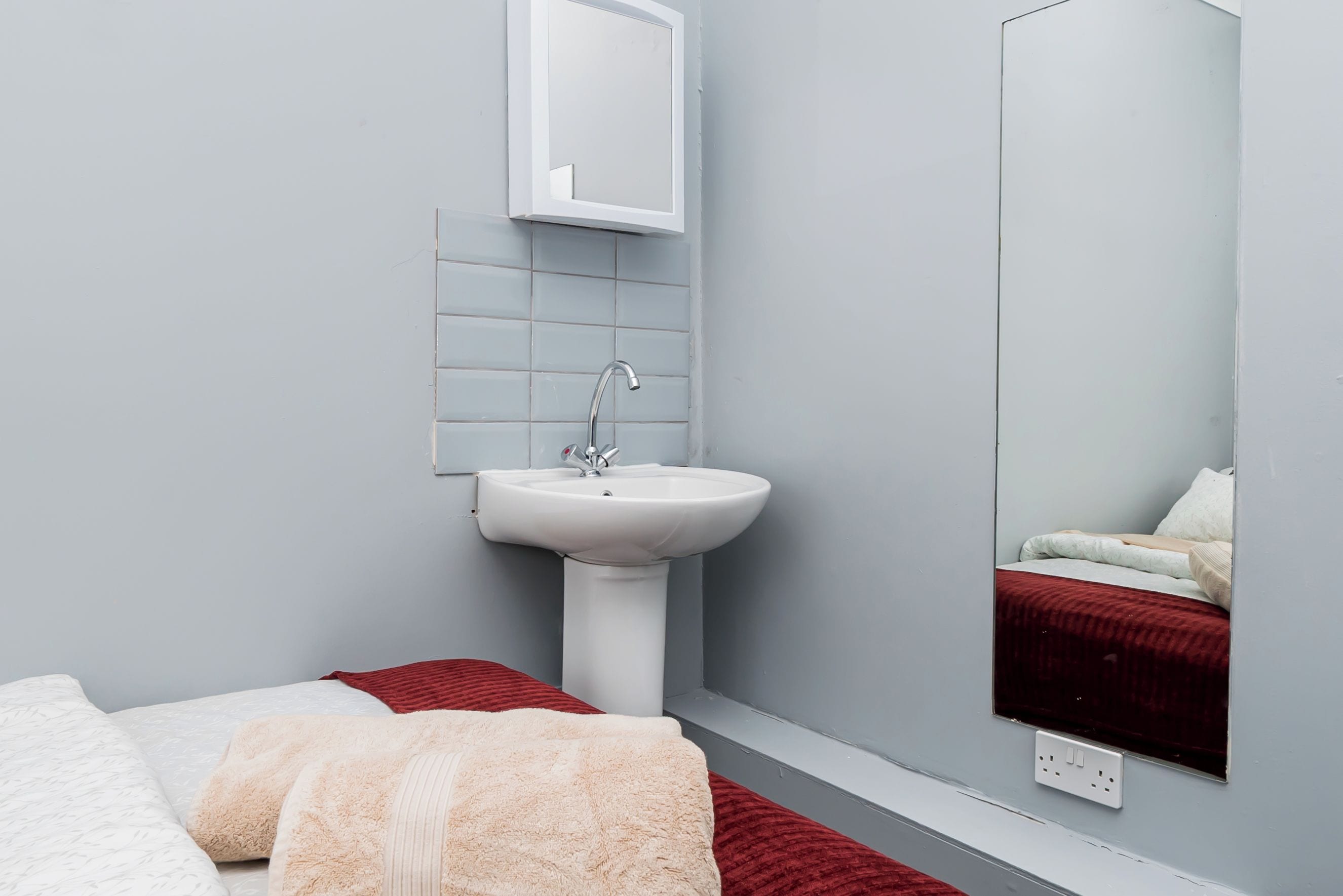 A modern bathroom with a white sink, a mirror, and a bed with a red blanket.