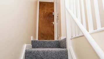 A staircase with a patterned carpet leading to a wooden door with a brass handle.