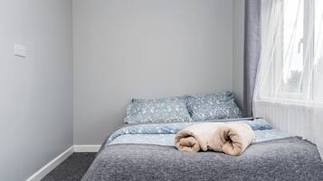 A bedroom with a bed, grey walls, a window with curtains, and a radiator.