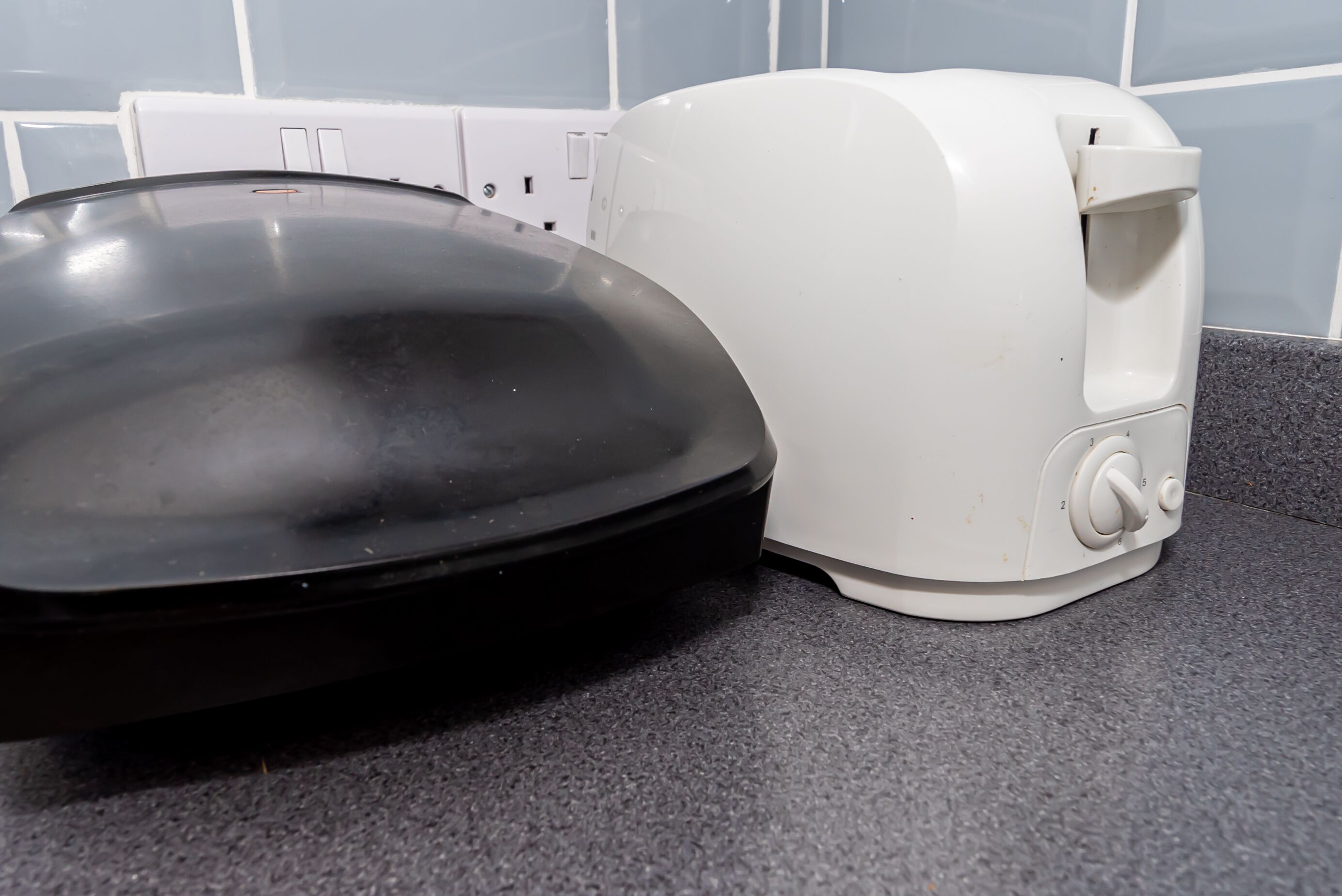 Eine Küche mit einer schwarzen Bratpfanne und einem weißen Toaster auf einer dunklen Arbeitsplatte.