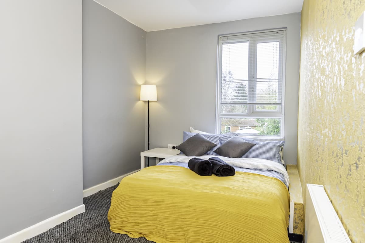 Een slaapkamer met een bed, nachtkastje, lamp en raam.