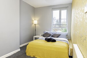 Un dormitorio con cama, mesita de noche, lámpara y ventana.